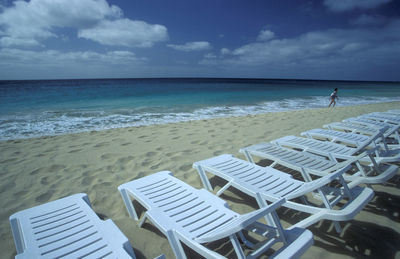 Deck chairs on beach against sky