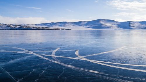 Frozen lake and mountains against sky during sunny day