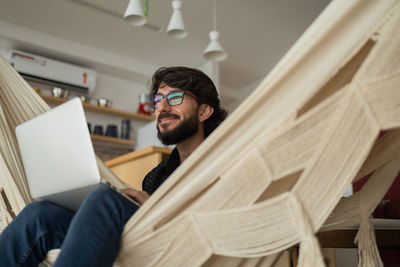 Young man  black glasses working with laptop on a white hammock notebook for working. home office