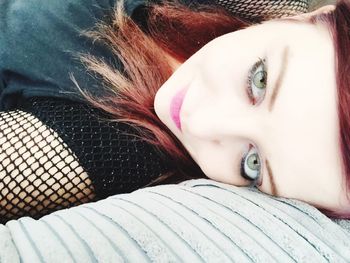 High angle portrait of young woman with green eyes lying on bed