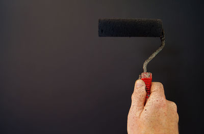 Close-up of hand holding paint roller against gray background