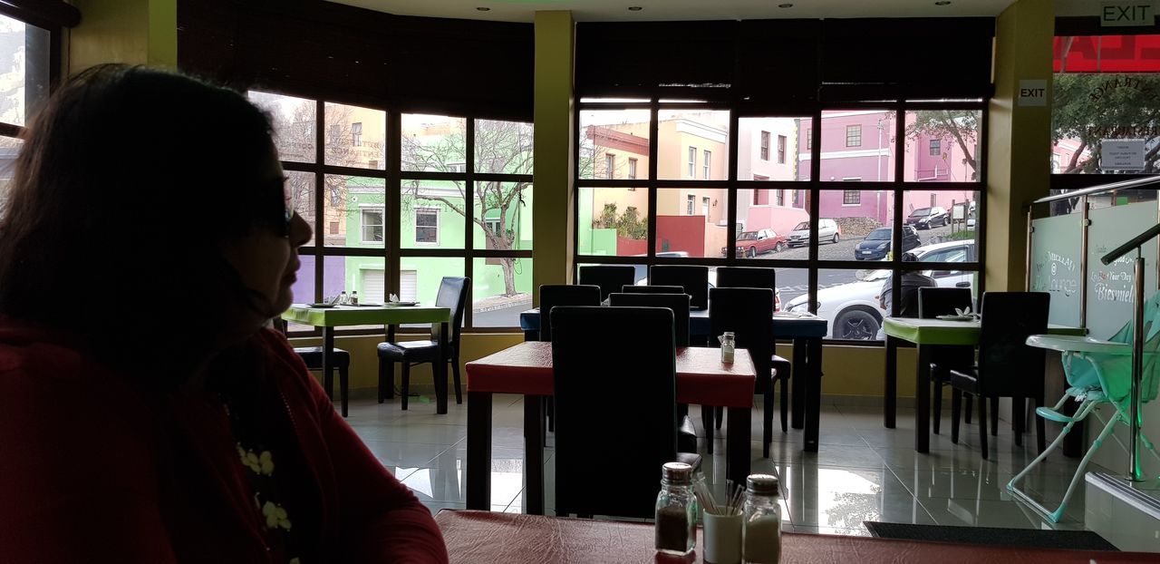 REAR VIEW OF WOMAN LOOKING THROUGH GLASS WINDOW