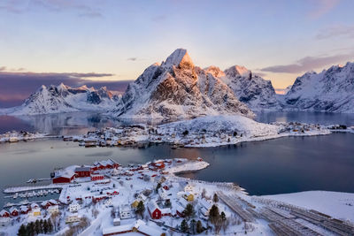 Frozen lake by snowcapped mountain against sky during sunset