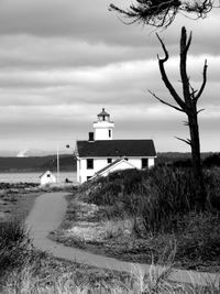 Bare tree and lighthouse on grassy field against cloudy sky