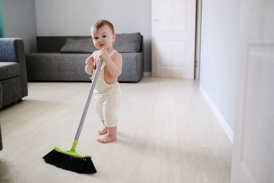 Toddler 1 year old with broom sweeps floor in bright room in scandinavian style, montessori 