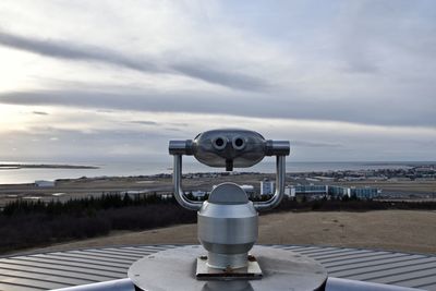 Coin-operated binoculars by sea against cloudy sky