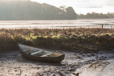 Abandoned boat moored on shore against sky
