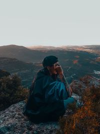 Man sitting on mountain against clear sky