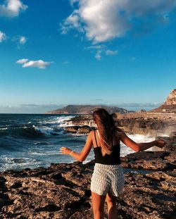 Rear view of woman standing at beach against sky