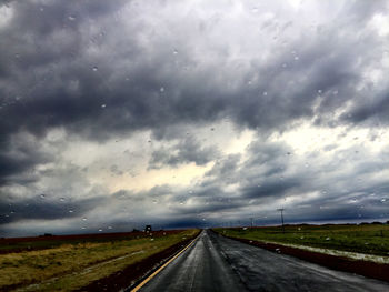 Road passing through field against cloudy sky