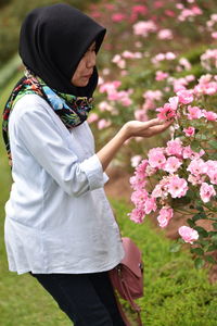 Side view of young woman looking pink flowers at park
