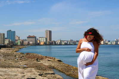 Young woman standing by sea against sky in city