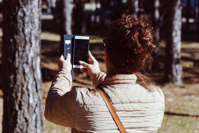 Rear view of woman photographing with mobile phone in forest