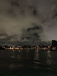 Illuminated city by sea against sky at night