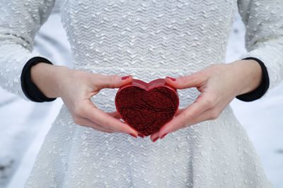 Selective focus of woman in white blouse holding a red heart-shaped box in her hands
