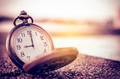 Close-up of pocket watch on retaining wall against sky