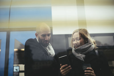 Business people using mobile phone while standing against tram