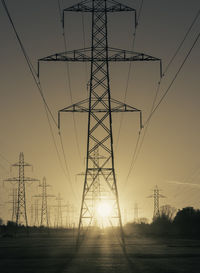 Low angle view of electricity pylon against sky during sunset