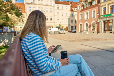 Rear view of woman using mobile phone in city
