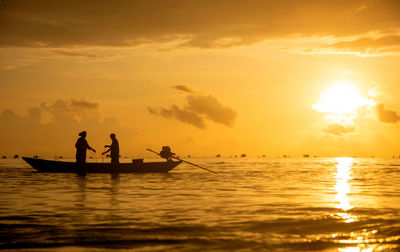 Silhouette fishermen on wooden boat preparing casting a net catching fish in the early morning