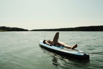 Woman lying down on surfboard over lake against sky