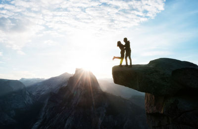 Men standing on rock by mountain against sky