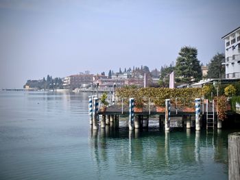 Wooden posts in river by buildings against sky