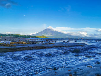 Scenic view of sea and snowcapped mountains against blue sky