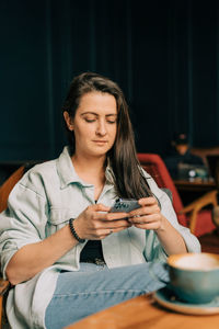 Young brunette woman sitting in coffee shop uses mobile phone for online messages.
