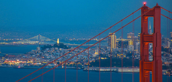 Illuminated city by sea against sky at night