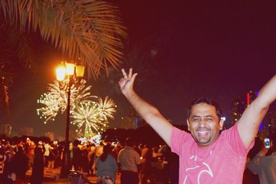 Happy man with arms raised standing against firework display at night