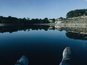 Low section of person by lake against sky