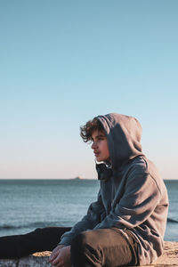 Side view of man sitting on shore against clear sky