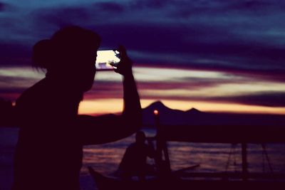 Silhouette of woman photographing through smart phone at sunset