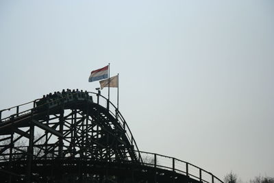 Low angle view of roller coaster against clear blue sky