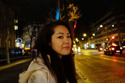 Portrait of young woman standing in city at night