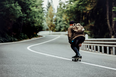 Rear view of man skateboarding on road