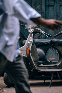 Midsection of man walking against motor scooter on road