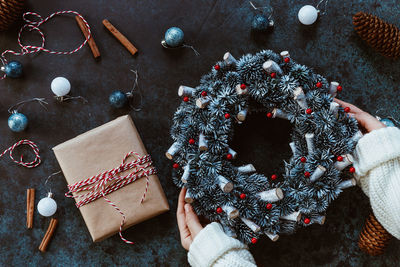 Cropped hand of person holding wreath by gift and christmas decoration