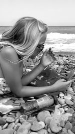 Midsection of woman sitting on pebbles at beach against sky