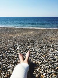 Low section of woman on pebbles at beach against sky during sunny day