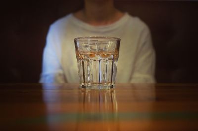 Midsection of woman sitting in front of empty glass on table