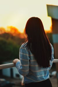 Rear view of woman standing against sky during sunset