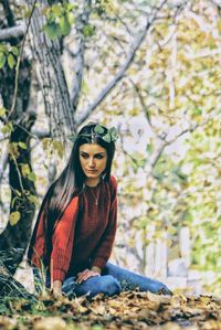 Sad young woman looking away while sitting in forest during autumn