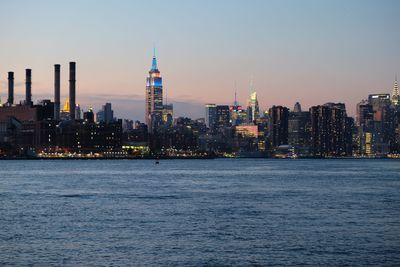 Illuminated empire state building and cityscape by river during dusk