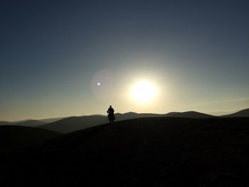 Silhouette man riding motorcycle on mountain against sky during sunrise