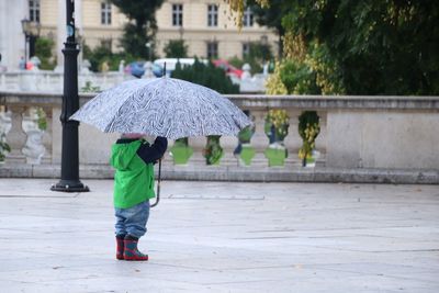 Rear view of woman with umbrella on street during rainy season