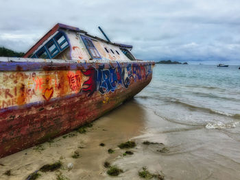 Abandoned boat on beach against sky