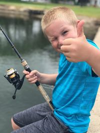 Portrait of cute boy showing thumbs up while fishing in lake