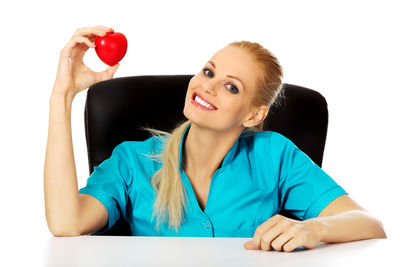 Portrait of smiling nurse holding heart shape against white background